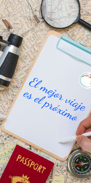 Libreta con el lema «El mejor viaje es el próximo» sobre un mapa, con pasaporte, brújula y prismáticos
